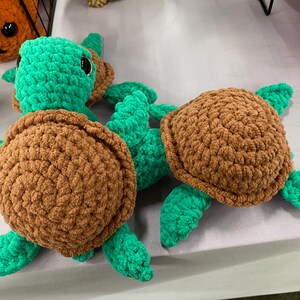 May include: Crocheted turtle toys in shades of brown and green. The turtles have textured shells and flipper-like limbs. The toys are handmade and appear soft and cuddly. The image shows multiple turtles, suggesting a collection or set.