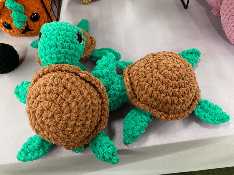 May include: Crocheted turtle toys in shades of brown and green. The turtles have textured shells and flipper-like limbs. The toys are handmade and appear soft and cuddly. The image shows multiple turtles, suggesting a collection or set.