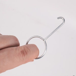 Könnte beinhalten: Ein silberner Metallhaken mit einer runden Schlaufe am Ende. Der Haken ist zum Aufhängen von Gegenständen gedacht.