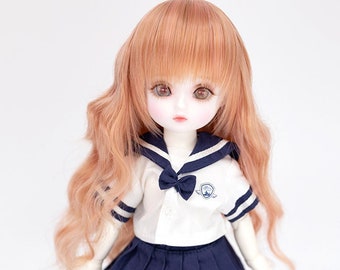 May include: A doll wearing a white sailor uniform with a blue skirt and a blue bow tie. The doll has long, wavy, light brown hair and is wearing black shoes.