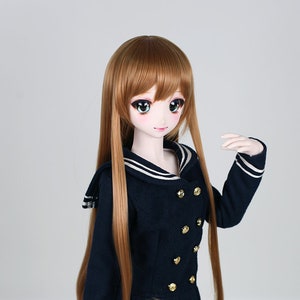 May include: A doll with long brown hair wearing a navy blue sailor dress with white trim and gold buttons. The doll has blue eyes and a light pink complexion.