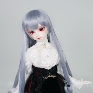 Puede incluir: Una muñeca con el pelo largo, liso y plateado, que lleva una blusa blanca de encaje con una falda negra de encaje y terciopelo. La muñeca tiene ojos rojos y una cara delicada.