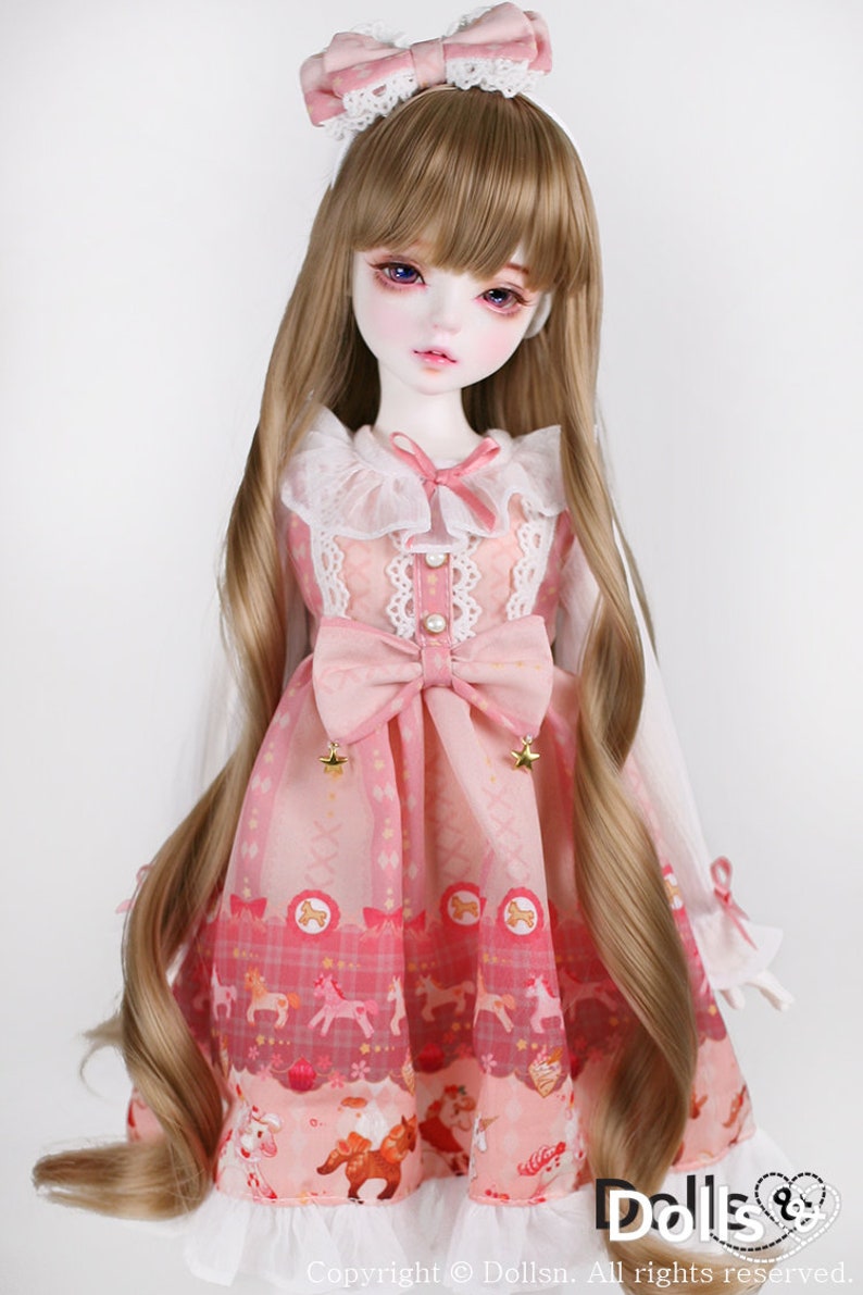 May include: A doll with long, light brown hair wearing a pink dress with a white lace collar and a pink bow. The dress has a pattern of horses and stars. The doll is wearing a pink bow headband.