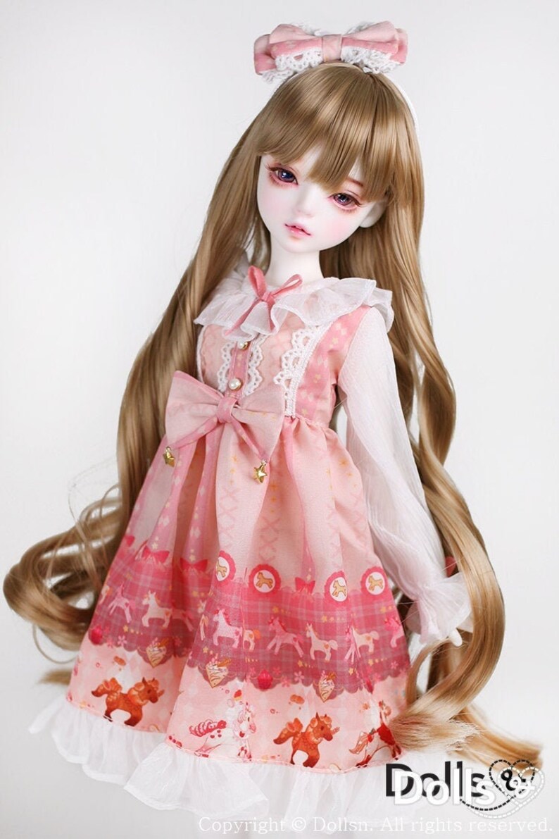 May include: A porcelain doll with long, wavy, light brown hair wearing a pink dress with a white lace collar and a white bow. The dress has a pink and white checkered pattern with a small horse design. The doll is wearing a pink bow headband.