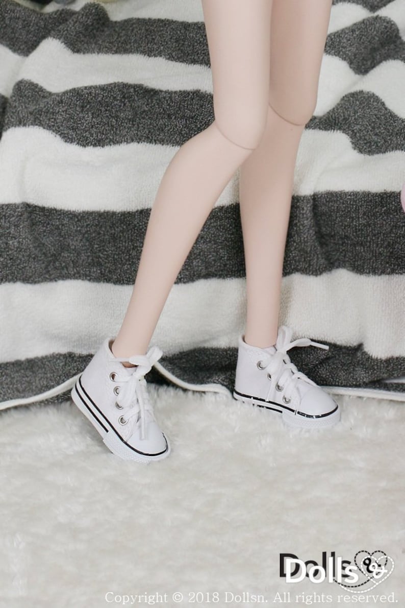 May include: White canvas high-top sneakers with black laces and a black trim around the sole. The sneakers are on a white fuzzy surface.