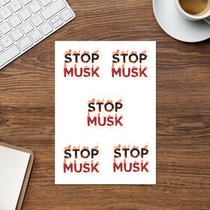 Könnte beinhalten: Fünf weiße Aufkleber mit dem Text "STOP MUSK" in schwarzen Buchstaben mit orangefarbenen Flammen hinter den Buchstaben. Die Aufkleber sind in zwei Reihen mit je zwei und einem in der Mitte angeordnet.