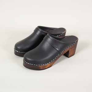 Pode incluir: Sapatos de couro preto com salto de madeira e detalhe de costura branca. Os sapatos têm uma tira de couro preto na parte superior com o nome da marca "ILSE CORK" gravado na tira.