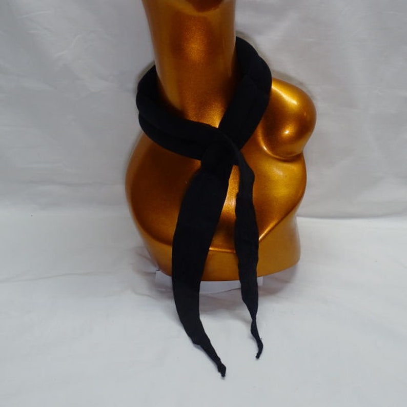 Puede incluir: Una bufanda negra est&aacute; drapeada alrededor de un maniqu&iacute; dorado. La bufanda est&aacute; hecha de un material suave y tiene extremos largos y puntiagudos. La bufanda est&aacute; envuelta alrededor del cuello del maniqu&iacute; y cuelga por delante.