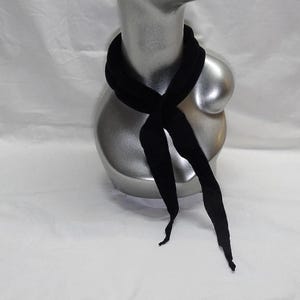 Puede incluir: Una bufanda negra est&aacute; drapeada alrededor de un maniqu&iacute; plateado. La bufanda est&aacute; hecha de un material suave y est&aacute; anudada en la parte delantera, con los extremos colgando. El fondo es una superficie blanca lisa.