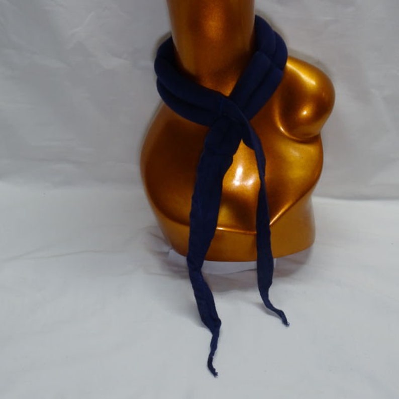 Puede incluir: Una bufanda azul marino est&aacute; drapeada alrededor de un maniqu&iacute; dorado. La bufanda est&aacute; hecha de un material suave y est&aacute; anudada en la parte delantera, con extremos largos y fluidos. El color oscuro de la bufanda contrasta con el tono dorado del maniqu&iacute;.