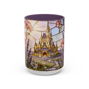 May include: White ceramic mug with a stained-glass design featuring a golden castle, pink flowers, and a purple interior. The design wraps around the mug, showcasing a whimsical landscape with a pathway and flowers.
