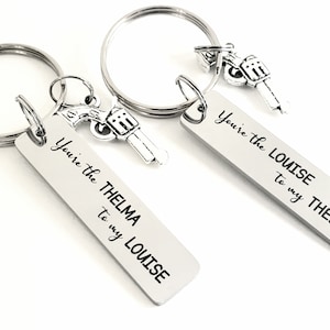May include: Two silver keychains with gun charms. One keychain has a tag that reads "You're the THELMA to my LOUISE". The other keychain has a tag that reads "You're the LOUISE to my THELMA".