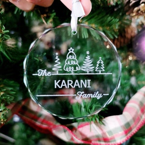 May include: A clear glass Christmas ornament with an etched design of four stylized Christmas trees and the text "The Karani Family".