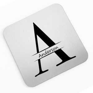 May include: A silver square coaster with a black stylized letter A and the name "Anderson" printed in black across the center.