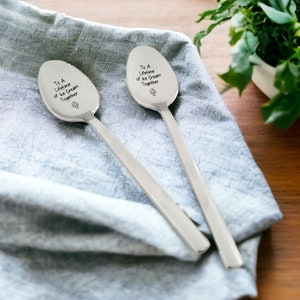 May include: Two silver spoons with the inscription "To a Lifetime of Ice Cream Together" on a blue cloth background.