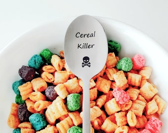 May include: A silver spoon with the words "Cereal Killer" and a skull and crossbones engraved on it. The spoon is resting in a bowl of colorful cereal.