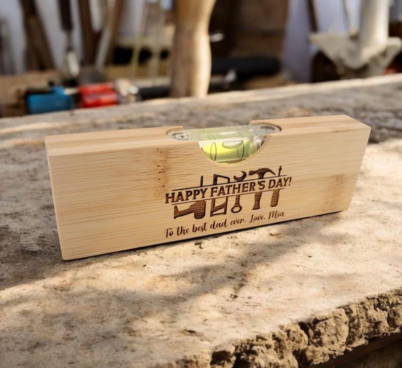 May include: A wooden level with a clear bubble vial. The level is engraved with the text "HAPPY FATHER'S DAY!" and a collection of tools. The inscription reads "To the best dad ever. Love, Mia."