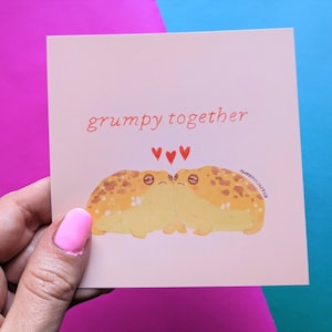 May include: A pink card with two yellow frogs with brown spots, facing each other. The frogs have red hearts above them and the text "grumpy together" is written in red.