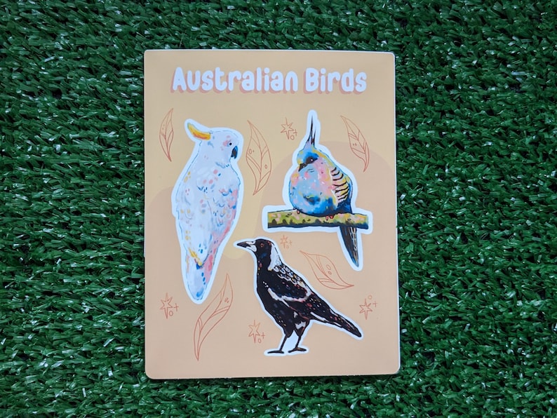 May include: A sheet of stickers featuring three Australian birds: a white cockatoo, a blue and pink bird, and a black and white magpie. The stickers are on a light orange background with a title that reads "Australian Birds".