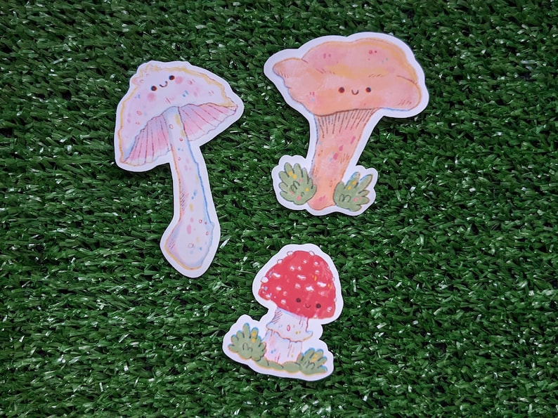 Peut inclure: Trois autocollants de champignons de dessin anim&eacute; mignons avec des visages heureux. Les champignons sont roses, orange et rouges avec des points blancs. Les autocollants sont parfaits pour ajouter une touche de fantaisie &agrave; votre agenda, votre ordinateur portable ou votre bouteille d'eau.