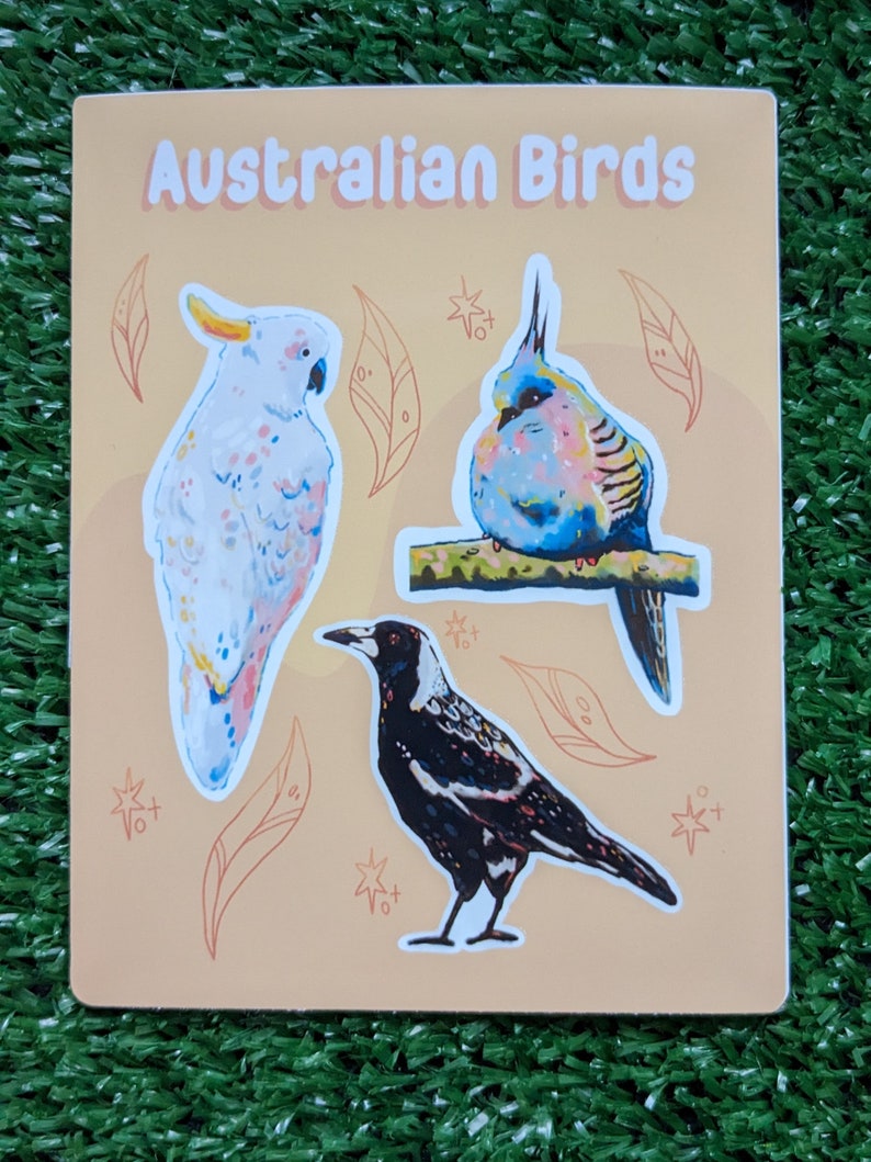 May include: A sticker sheet featuring three Australian birds: a white cockatoo, a blue and pink bird, and a black and white magpie. The sticker sheet has a light orange background with brown leaves and white stars.