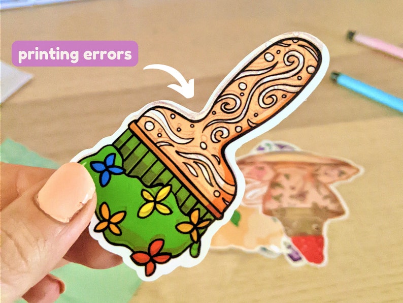May include: A green paintbrush sticker with a floral design and a brown handle with a swirl pattern. The sticker has the words "printing errors" written on it.