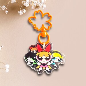 May include: A silver keychain featuring the Powerpuff Girls, Blossom, Bubbles, and Buttercup, with a bright orange plastic key ring.