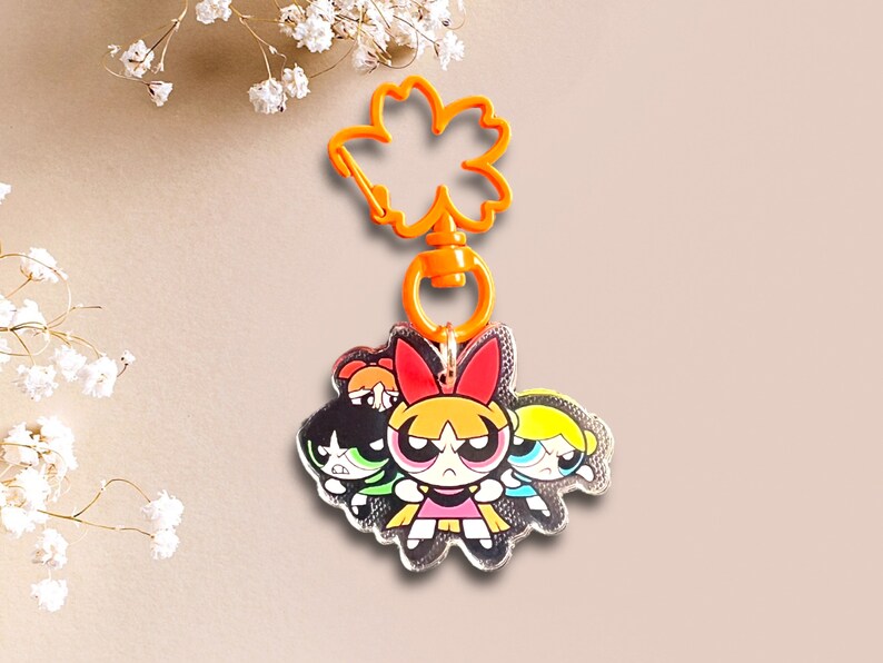 May include: A silver keychain featuring the Powerpuff Girls, Blossom, Bubbles, and Buttercup, with a bright orange plastic key ring.