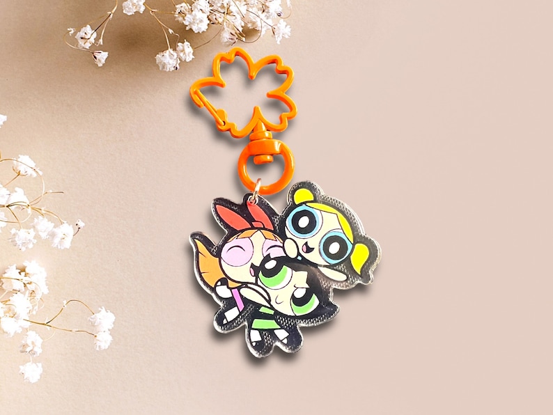 May include: A colourful keychain featuring the Powerpuff Girls, Blossom, Bubbles, and Buttercup, with a bright orange plastic clasp.