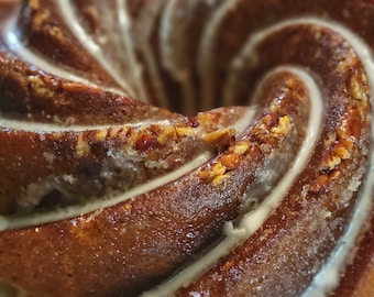May include: A close-up of a bundt cake with a white glaze and a swirl pattern. The cake is covered in a light brown glaze and has a slightly crunchy texture.