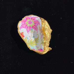 May include: A small, gold-painted, ceramic bowl with a floral pattern inside. The bowl is shaped like a seashell and has a white background with pink, green, and blue flowers.