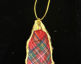 May include: A gold-painted oyster shell ornament with a red, green, and blue plaid fabric inside. The ornament has a gold string for hanging.