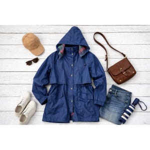 May include: A flat lay of a navy blue hooded raincoat, brown purse, blue jeans, white sneakers, a tan baseball cap, sunglasses, and a striped umbrella. The raincoat has a drawstring waist and a plaid lining in the hood.