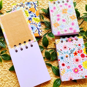 May include: Four small spiral bound notebooks with floral patterns. The notebooks have white pages and are perfect for jotting down notes, ideas, or lists.