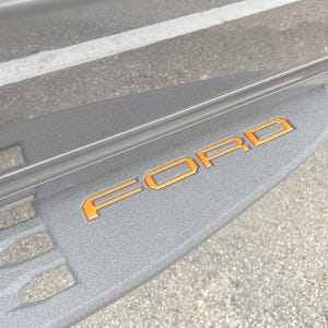 Puede incluir: Primer plano de un escalón texturizado gris con la palabra "FORD" en letras naranjas.