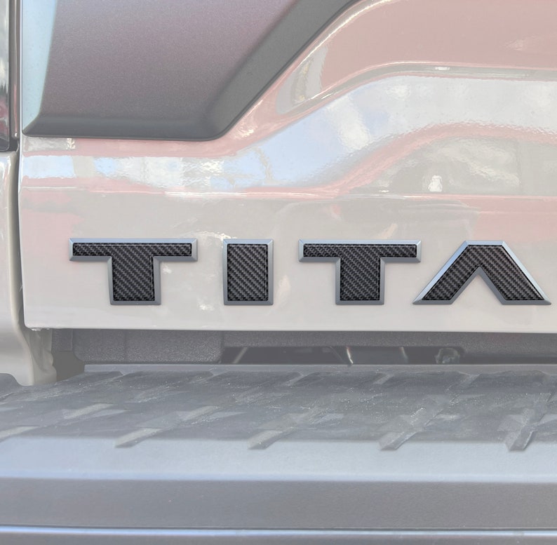 May include: A close-up of a silver truck tailgate with a black carbon fiber "TITAN" emblem.