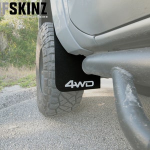 Peut inclure: Gros plan sur un garde-boue noir avec un logo "4WD" blanc sur un camion argenté. Le garde-boue est fixé au passage de roue arrière du camion. Le camion est garé sur un chemin de gravier.