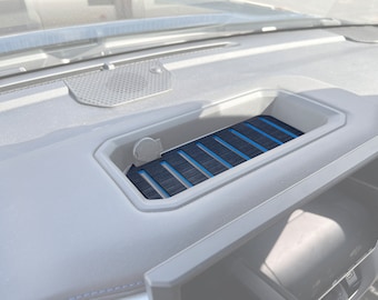 May include: A gray car dashboard with a black and blue textured tray. The tray has a small, round, gray button on the left side.