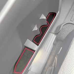 Könnte beinhalten: Schwarze und rote Zubehörteile für die Innenausstattung des Autos. Das Set enthält drei passgenaue Matten zum Schutz des Fahrzeuginnenraums. Die Matten haben eine schwarze Oberfläche mit rotem Rand und sorgen für einen kontrastreichen und stilvollen Look. Das Zubehör ist für bestimmte Bereiche des Autos konzipiert.