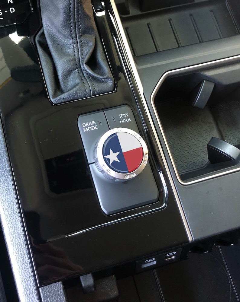May include: A close-up of a car's interior showing a black and silver drive mode knob with a Texas flag design. The knob is labelled "Drive Mode" and "Tow/Haul".