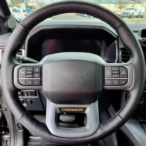 May include: A black leather steering wheel with a silver trim and a "TREMOR" badge. The steering wheel has buttons for controlling the vehicle's functions.
