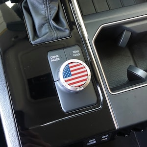 May include: Close-up of a car's centre console with a drive mode knob featuring an American flag design. The knob is labelled "Drive Mode" and "Tow/Haul".