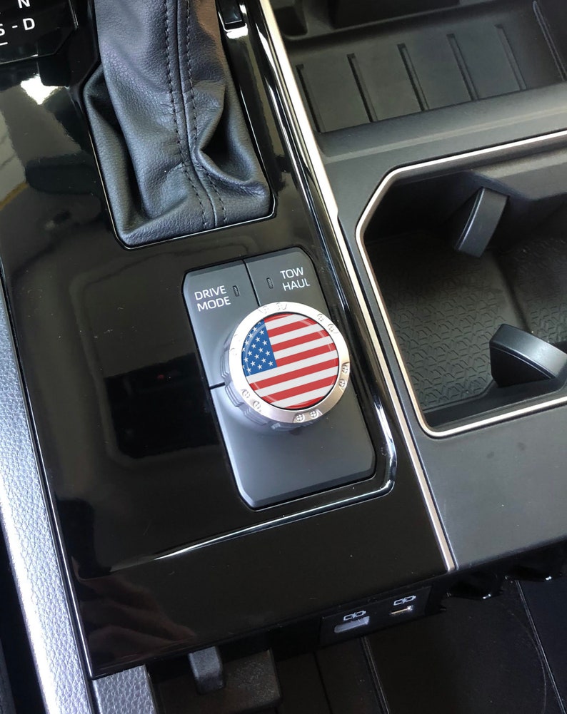 May include: Close-up of a car's centre console with a drive mode knob featuring an American flag design. The knob is labelled "Drive Mode" and "Tow/Haul".