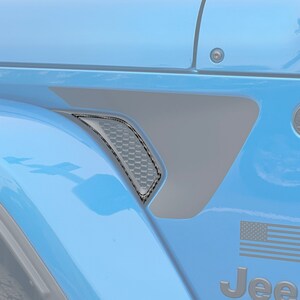 May include: A blue Jeep Wrangler with black fender flares and a black American flag decal. The Jeep has a black "Jeep" logo on the side.
