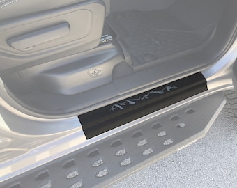 May include: Black door sill protector with a mountain range design. The protector is installed in a vehicle's door frame. The step has a textured surface and a silver vehicle frame.