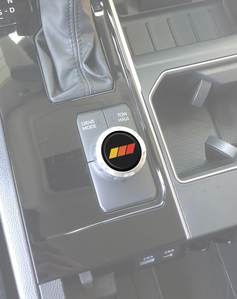 May include: A silver knob with a black centre and a red, orange and yellow stripe design. The knob is labelled "Drive Mode", "Tow", and "Haul".