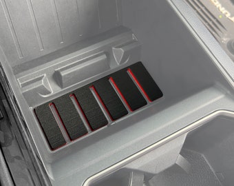 May include: A black car interior with a gray plastic storage compartment. The compartment has five black rubber inserts with red lines.