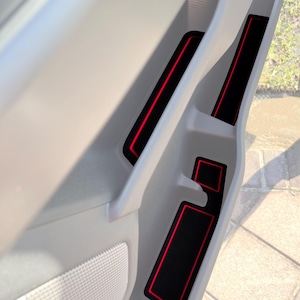 May include: Black car door storage liner with red trim. The liner is made of a soft, durable material and helps to keep your car clean and organized.
