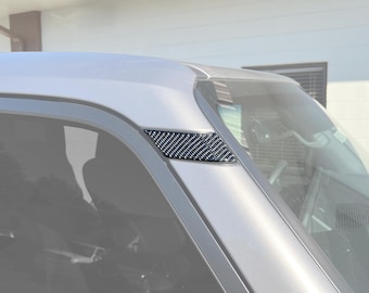 May include: A close-up of a black carbon fiber trim piece for a car. The trim piece is installed on the side window of a vehicle.
