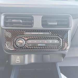 Puede incluir: Un salpicadero de coche con un embellecedor de fibra de carbono alrededor de la radio y los controles del climatizador. El salpicadero incluye rejillas de ventilación, un mando de volumen y botones de función. El texto "PASSENGER AIRBAG" es visible.